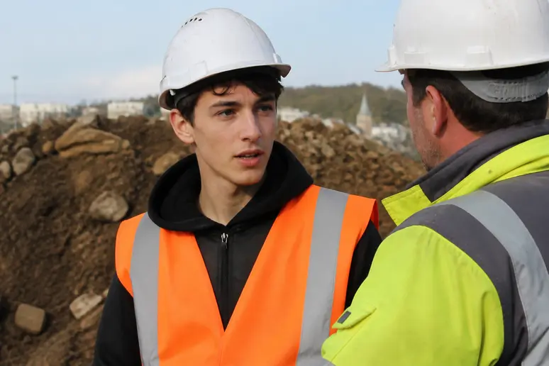 Apprenti sur un chantier dialogue avec un responsable, préparant son intégration professionnelle dans les travaux publics.