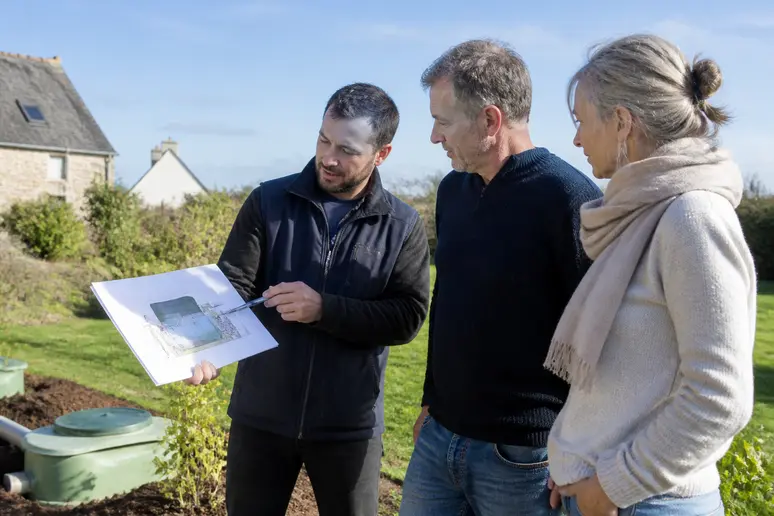 Un technicien explique un système de filtre compact à des propriétaires dans un jardin en Ille-et-Vilaine.