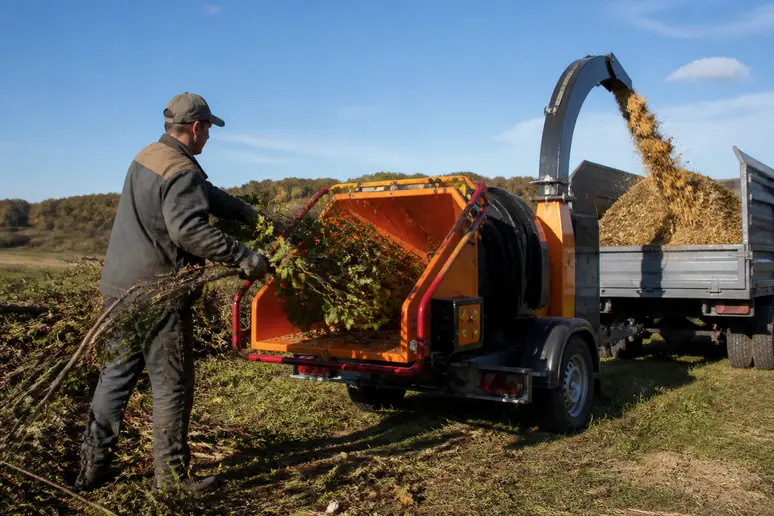 Agriculteur en Ille-et-Vilaine utilisant une déchiqueteuse mobile pour transformer des branches en copeaux de bois utiles.