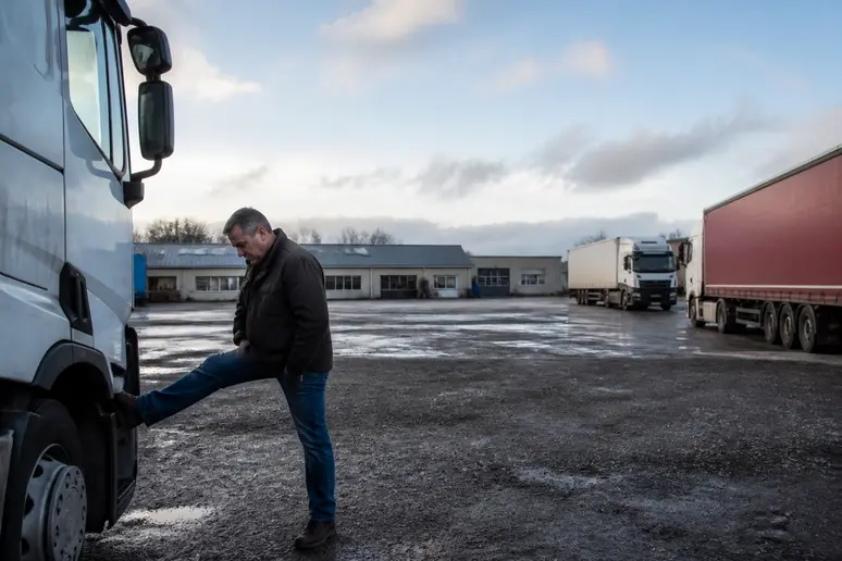 Un chauffeur routier s'étire près de son camion dans une aire de repos en Ille-et-Vilaine, reflétant le paysage économique du secteur.