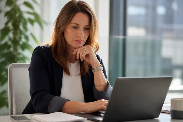 Une femme d'affaires française examine attentivement un plan de carrière sur son ordinateur portable dans un bureau moderne.