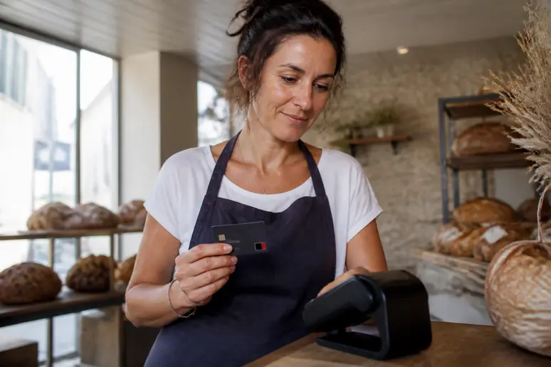Boulangère bretonne utilise sa carte bancaire professionnelle pour un paiement sur son terminal dans sa boulangerie artisanale.