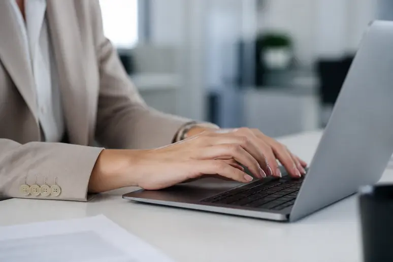 Mains d'une femme tapant sur un clavier d'ordinateur portable, gérant des démarches administratives en ligne.
