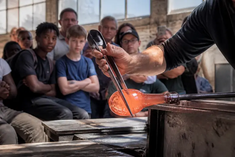 Des visiteurs observent un maître verrier travailler le verre en Ille-et-Vilaine, découvrant les métiers d'art.