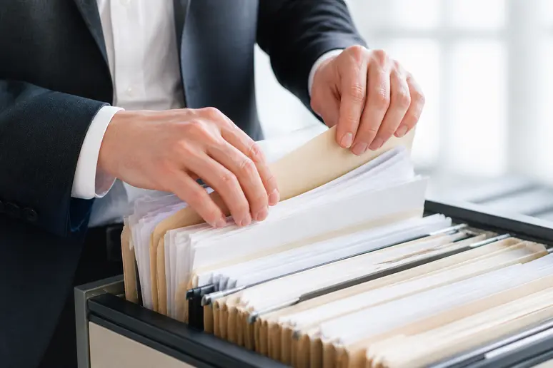 Mains triant consciencieusement des dossiers de contrats et justificatifs financiers dans un classeur.