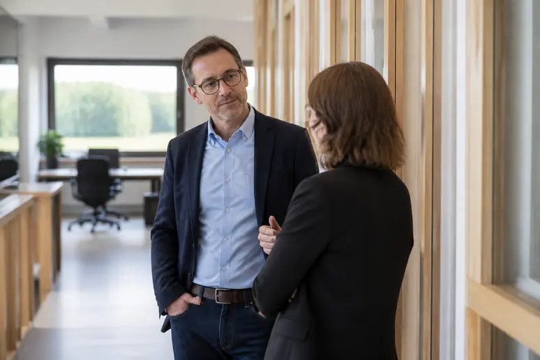 Deux collègues discutent debout dans le couloir d'un espace de coworking lumineux.