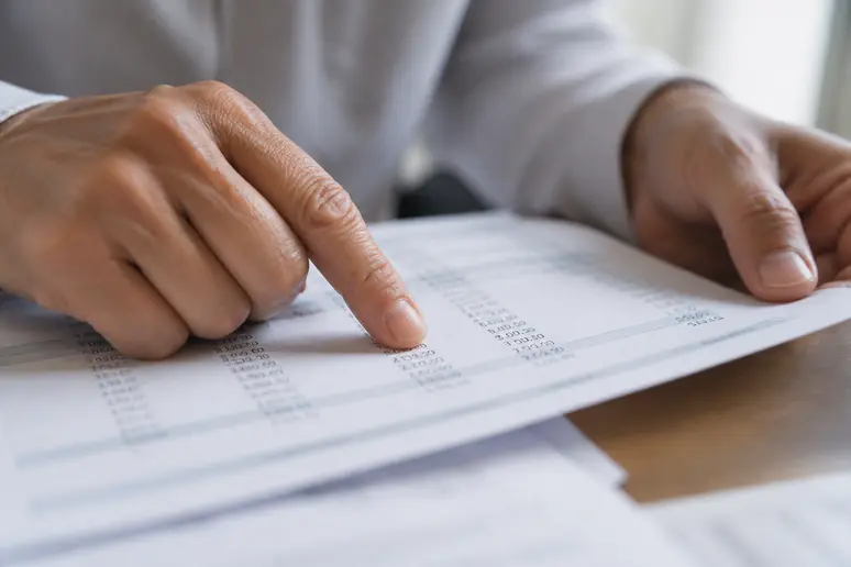 Doigts pointant les lignes chiffrées sur un bulletin de paie imprimé papier