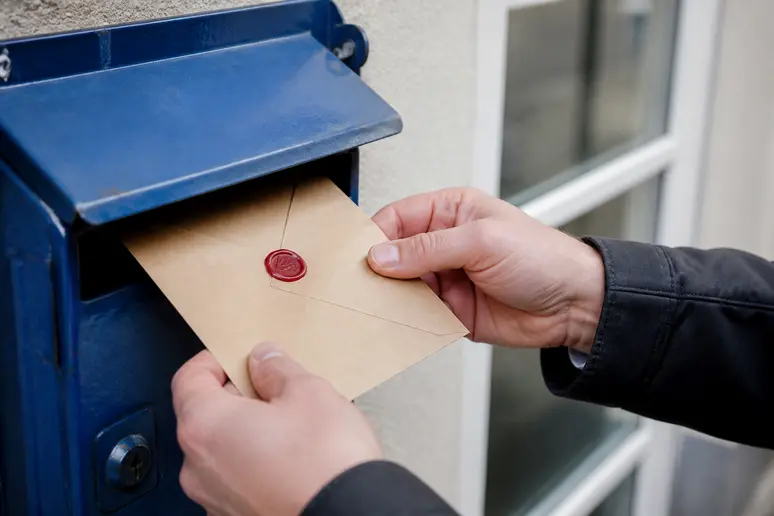 Mains insérant une lettre dans une boîte aux lettres pour un envoi recommandé.