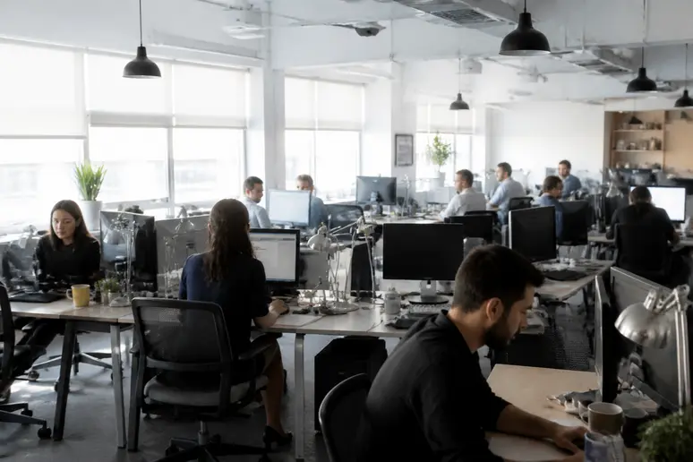 Espace de travail en open-space avec des collaborateurs travaillant sur des bureaux organisés.