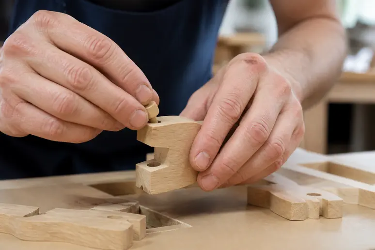 Mains d'un ouvrier assemblant avec précision des pièces en bois dans un atelier bien éclairé.