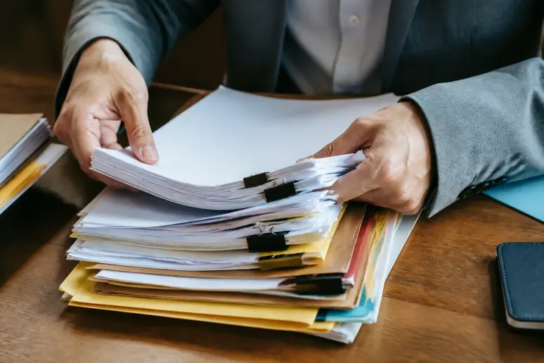 Mains triant des documents et des dossiers papier sur un bureau pour le suivi administratif