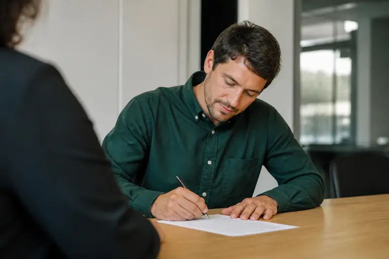 Un adulte en reconversion signe un contrat d'alternance sur un bureau en bois.