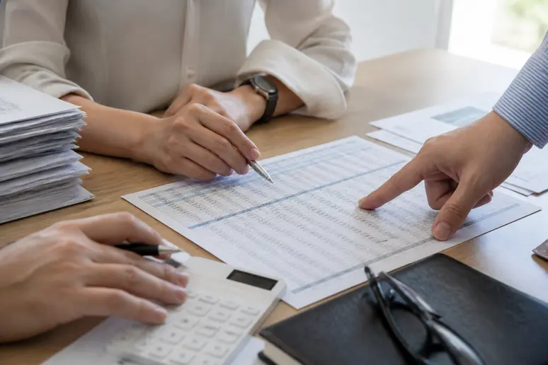 Des mains pointent un calcul d'heures supplémentaires sur un tableau de suivi d'entreprise.